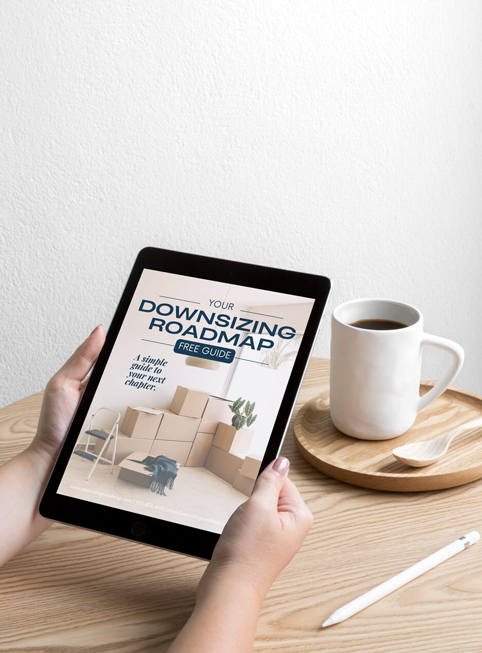 A woman holding an ipad while seated at a table with coffee. The ipad shows The Downsizing Roadmap Guide